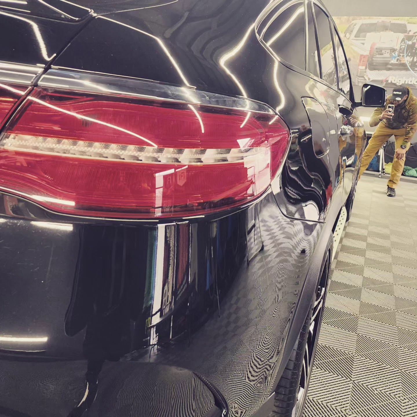 Close-up of black SUV taillight and body with detailer visible in reflection
